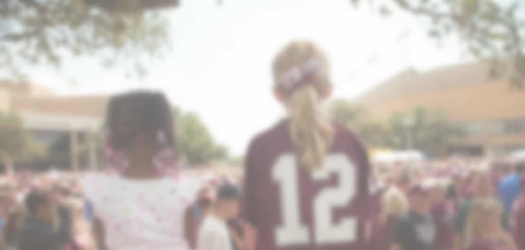 Two young girls with their backs to us look out at a crowd of sports fans.